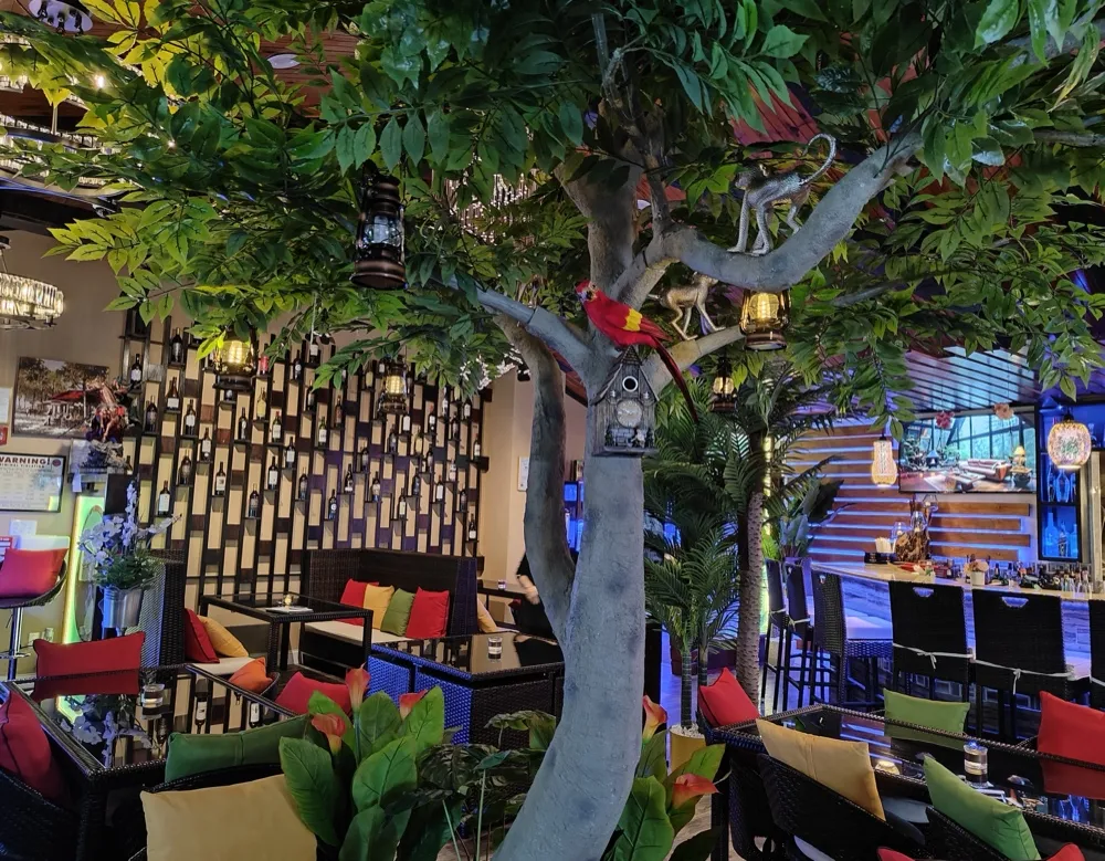 A leafy indoor tree with a monkey figurine and lanterns above the lounge seating