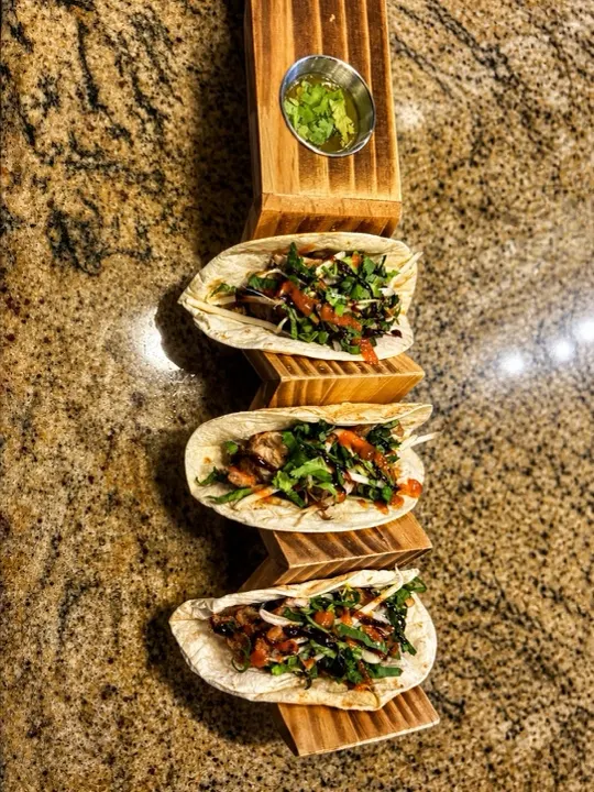 A row of fusion tacos filled with herbs and greens on a wooden holder